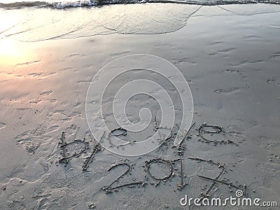 Handwritten words â€œbye bye 2017â€ on the beach with many footprints Stock Photo